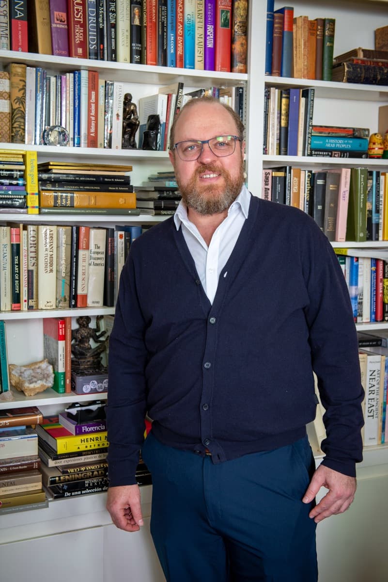 Max Koz standing in front of a full bookshelf, smiling.